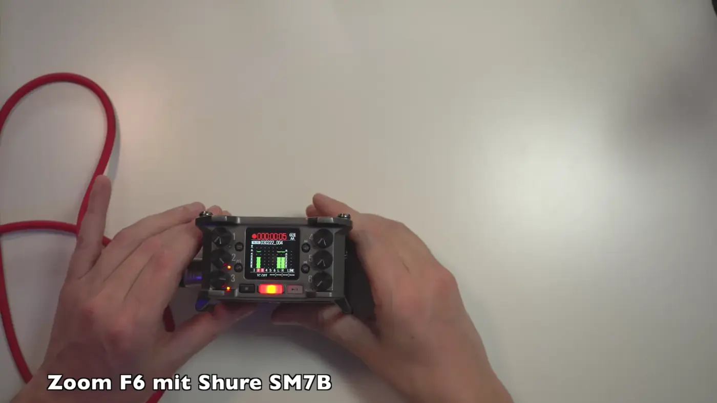 Zoom F6 in den Händen, angeschlossen an ein Shure SM7B, Display zeigt die Pegel